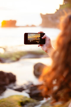 Man taking photo of seaside sunset with phone