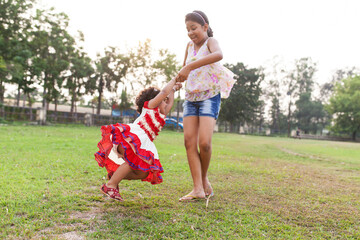 A teenager and a kid holding hand and making rotation in a green ground