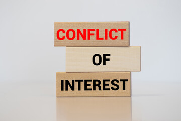 Male hand placing a block with word 'conflict' on top of a blocks tower with words 'conflict of interest'.