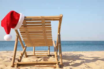 Sun lounger with Santa's hat on beach, space for text. Christmas vacation