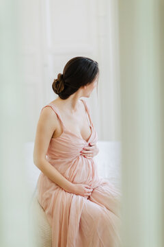 Intimate portrait through open doors of beautfiul mother-to-be sitting on her bed