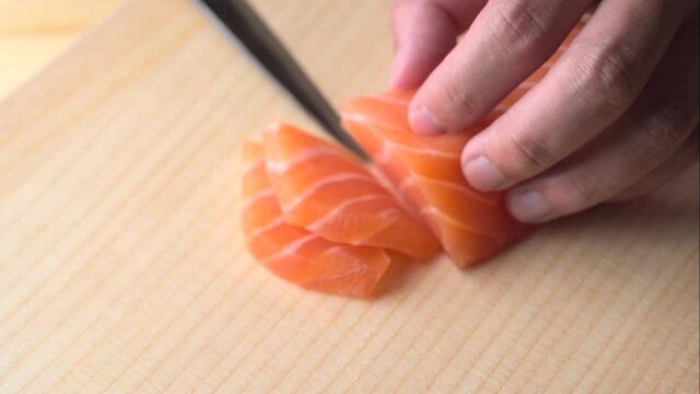 slicing salmon sashimi with knife on wooden cutting board