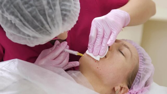 Cosmetologist makes the Rejuvenating facial injections procedure for tightening and smoothing wrinkles on the face skin of young woman in a beauty salon