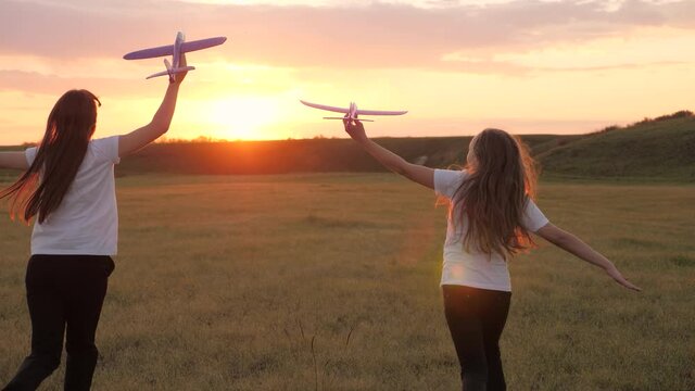 Children on background of sun with an airplane in hand. Silhouette of children playing on plane. Dreams of flying. Happy childhood concept. Two girls play with a toy plane at sunset.