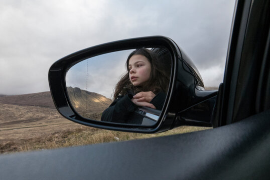 Reflection of girl in car mirror on road in Scottish Highlands
