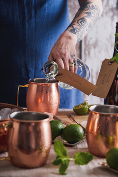 Woman pouring vodka into a copper mug, while preparing Moscow mule cocktails.