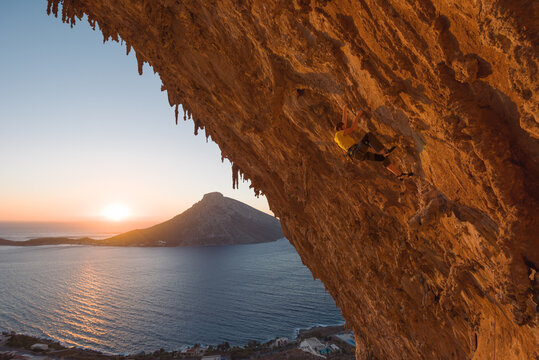 Man rock climbing on craggy rock wall during sunset