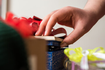 Hand opening a gift with a red ribbon and some other gifts on a table  