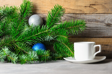 Fir branches with green needles, Christmas balls and a Cup of coffee on a saucer on a wooden background.
