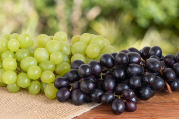 Green and purple grapes on wooden mes with blurred background.