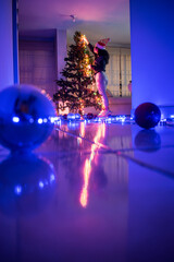 Girl making the christmas tree with some colorful lights and christmas balls at home 
