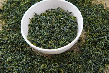 Dry green tea in a white cup on a sacking background