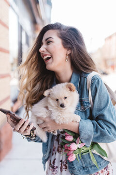 A beautiful young woman walking down a city street shopping with her dog