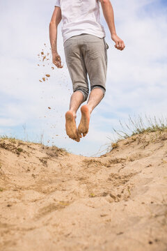 Young man flinging sand by jumping in the dunes.