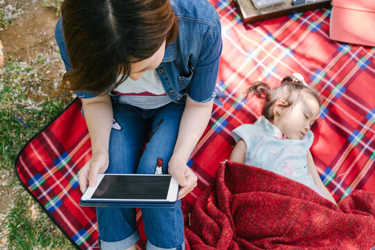 Adorable girl sleeping while her mother using iPad on a picnic mat
