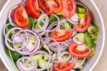 Closeup of a fresh salad with spinach, cucumbers, tomatoes, and red onions.