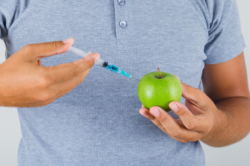 Young man conducting experiment by injection into apple in grey t-shirt , front view.