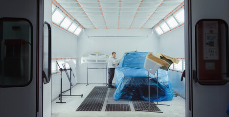 Worker/painter working on car bodywork in paint chamber/workshop.