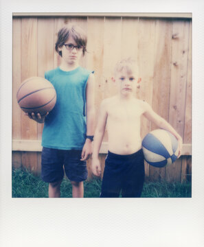 Brothers with basketballs in front of wood fence