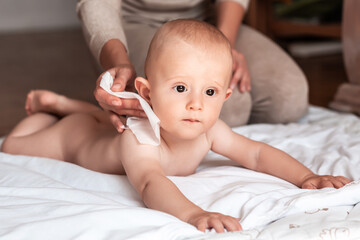 Hygiene - young mom wiping the baby skin body with wet wipes carefully. Mother changing the baby...