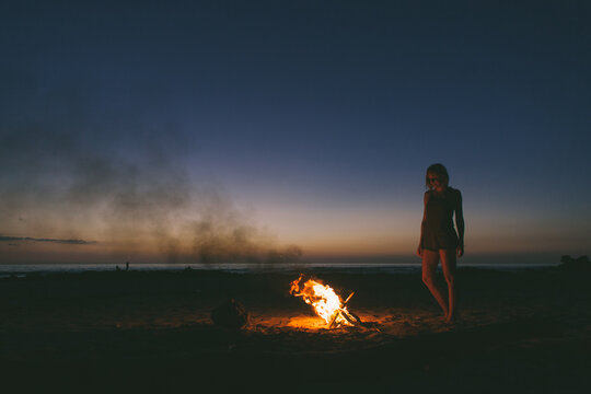 Woman enjoying the warmth of a bonfire on the beach under the stars.