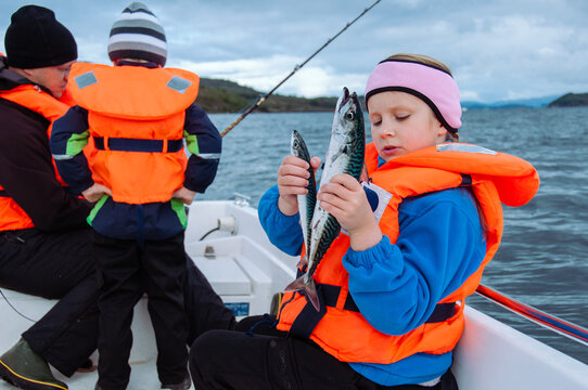 A girl in a fishing baot in a sea holding the mackerel as a catch of a day with the rest of a family om background