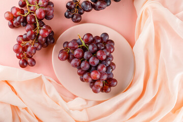 Red grapes in a plate flat lay on pink and textile background