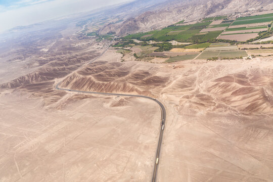 Airplane view of Panamericana cutting through hills to a green irrigated valey in Nazca Peru
