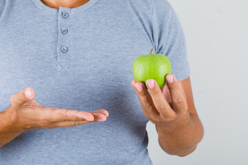 Young man holding green apple in grey t-shirt front view.