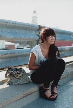 Fashionable young woman sitting and smiling near guardrail