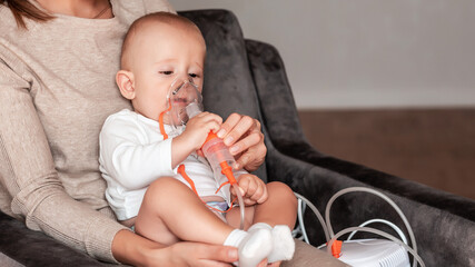 Baby taking respiratory therapy. Hand holding the mask of a nebuliser at home. symptom of asthma or...