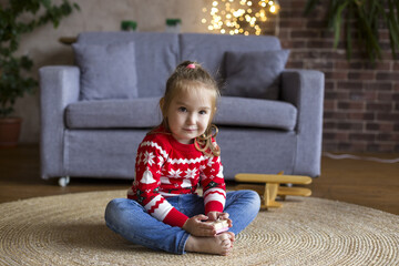 Little cute girl in red christmas sweater playing in the living room with gifts