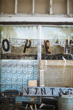 open sign hanging from wooden pegs from a wire matress