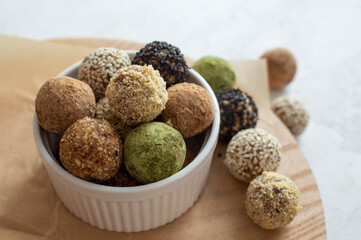 Homemade healthy vegan raw energy truffle balls in white bowl. Made with dried dates, walnuts, almonds and cashews in sesame seeds, matcha powder and carob. The concept of healthy and vegetarian food.