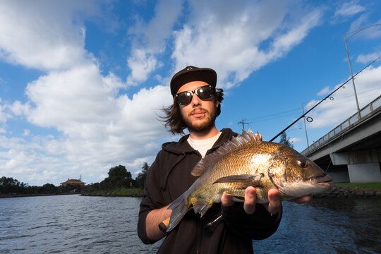 Young adult fisherman holding a bream