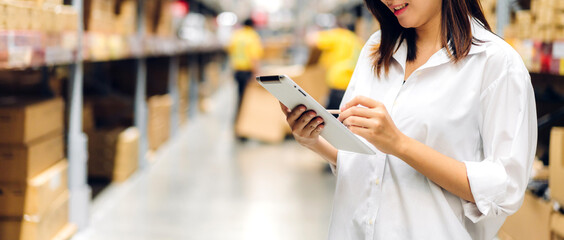 Portrait of smiling asian manager worker woman standing and order details on tablet computer for checking goods and supplies on shelves with goods background in warehouse.logistic and business export