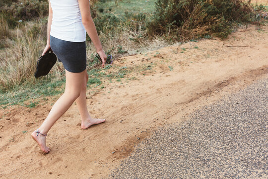 Legs of teenage girl, wearing a short skirt, walking barefoot along a road