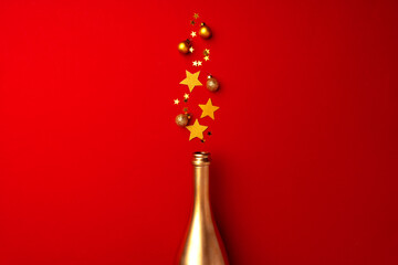 Champagne bottle with sparkling confetti on red background flat lay
