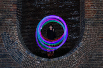 Glowing trails of light made by a Poi dancer using led glow poi's within the arches of a viaduct