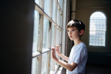 Boy stands looking out the window of an old building