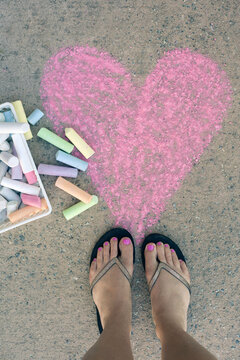 Girl's feet in flip flops with chalk and a big, pink heart