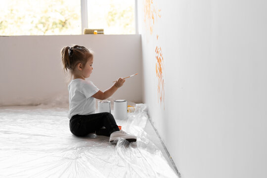 little girl with a brush in her hands draws on the wall. Home renovation concept.