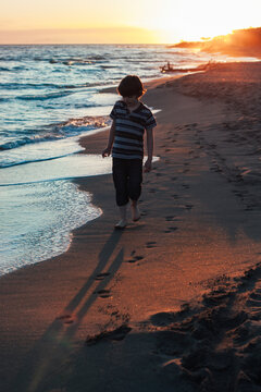 Boy walking away on the beach at Sunset