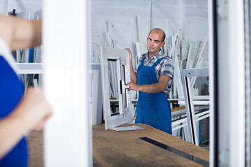 Portrait of positive male worker with finished plastic window in assembly shop