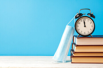 Stack of books with alarm clock and medical mask
