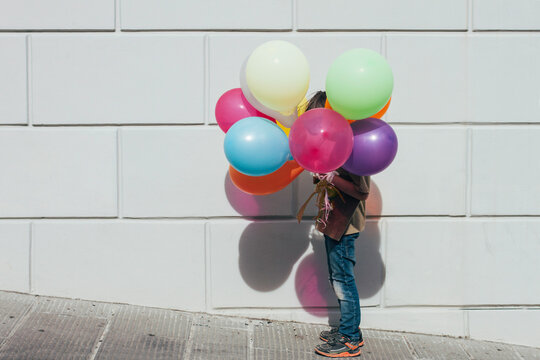 Boy holding balloons under the Sun on the street in front of a wall