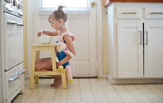 little girl dressed as ballerina with toy in kitchen