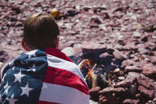 A boy wrapped in a towel sitting in front of a fire on a beach