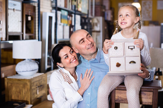 Cheerful positive family is holding new curbstone that their choosing for bedroom in the furniture store.
