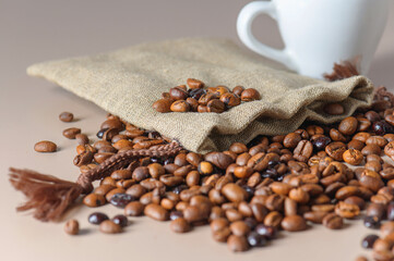 Roasted coffee beans, a white Cup, and a small burlap bag in close-up. Roasted coffee beans of the morning mood.